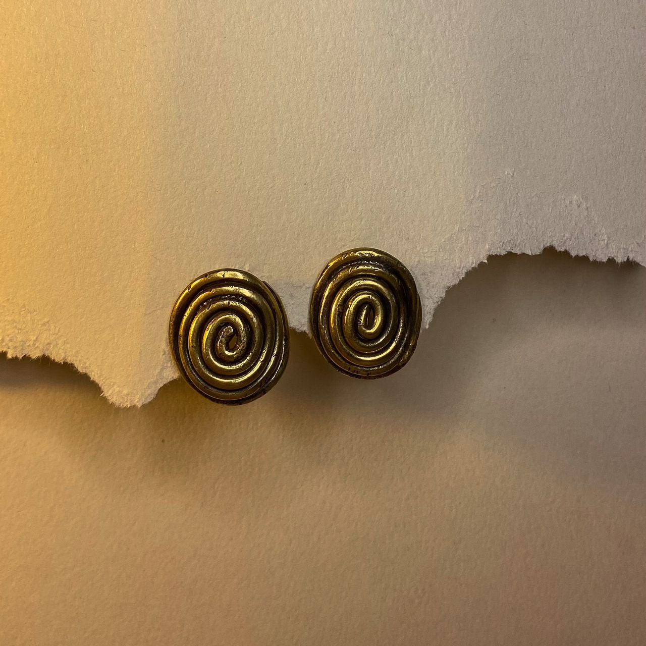 Pair of Brass spiral earrings on a textured beige surface